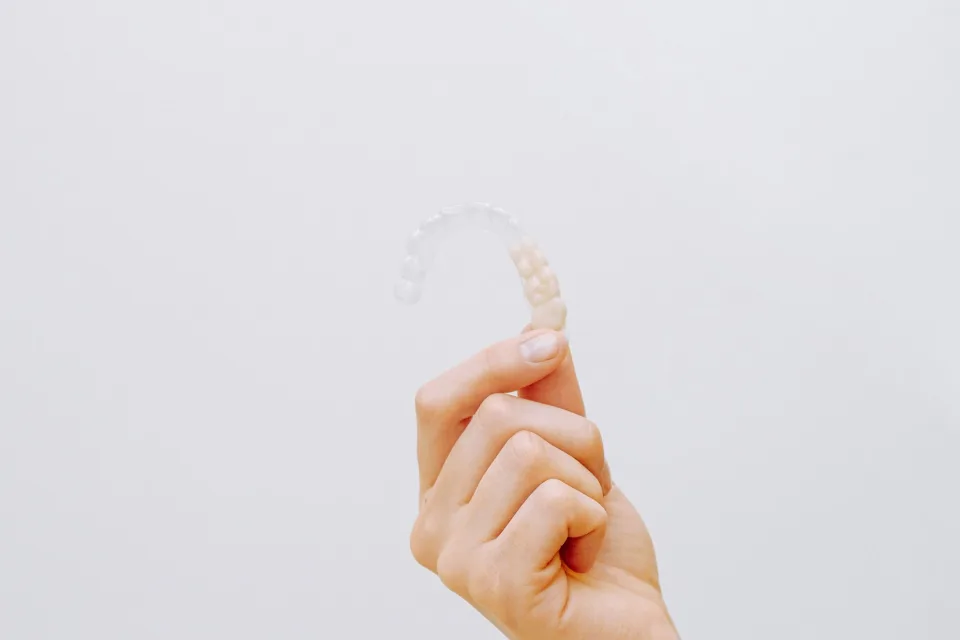 Hand holding a transparent clear aligner against a light background