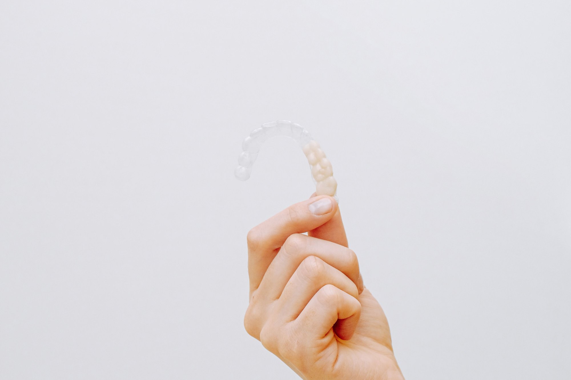 Hand holding a transparent clear aligner against a light background